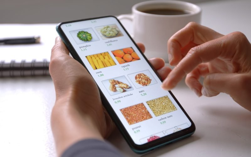 Woman using smartphone buys food online in the internet shop store. Woman's hand on the mobile phone screen selects the goods remotely at home .