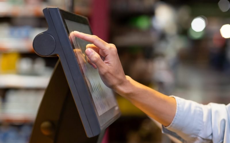 Close-up photo of a woman's hand in a supermarket inside using a self-service scale weighing vegetables and fruit in the store.