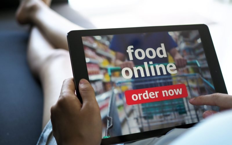 Women use tablets to order food online while lying on the couch at home.
